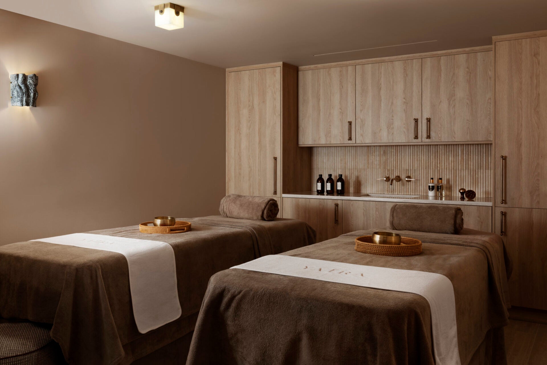 A pristine, fully equipped luxury hotel dual treatment room with beige accents, brass bowls, and fine wood cabinetry. COCON Group recruits elite spa professionals to work exclusively within Europe's most prestigious five-star hospitality environments.